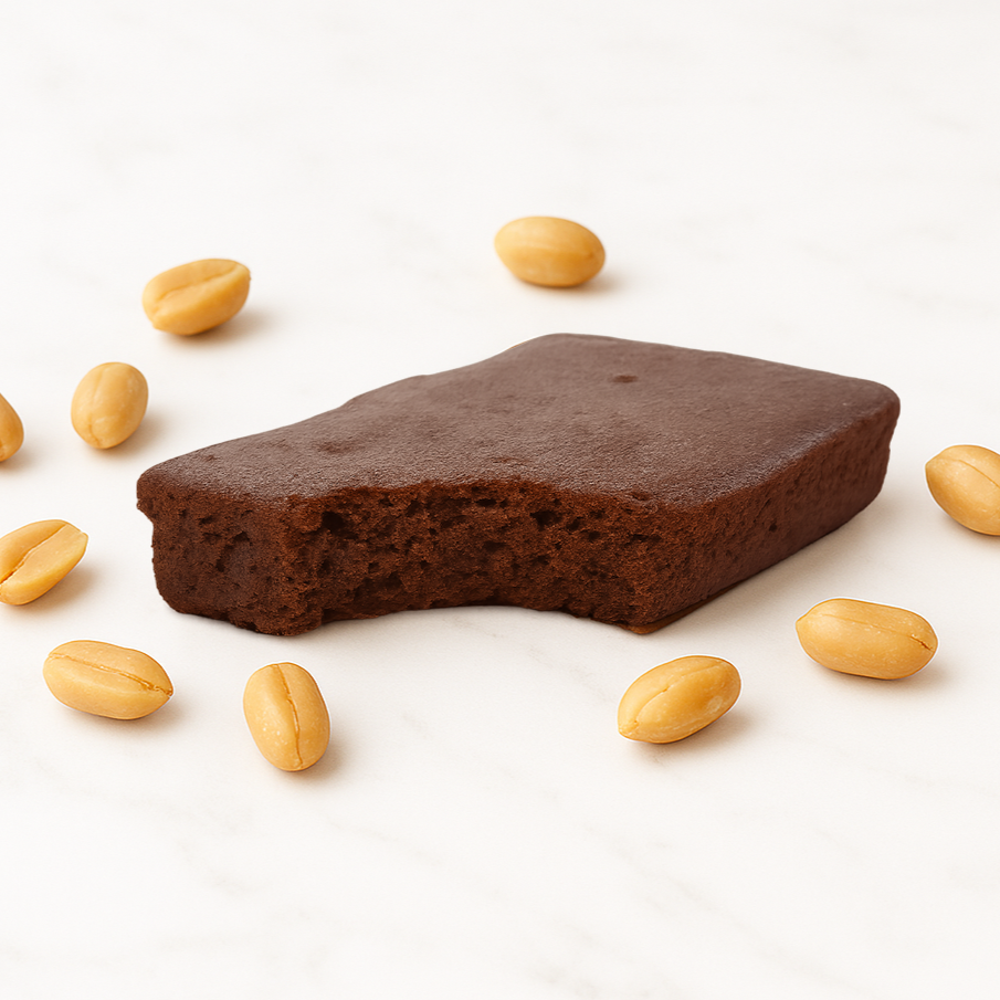 Protein Brownie with a bite taken out, surrounded by peanuts on a white background
